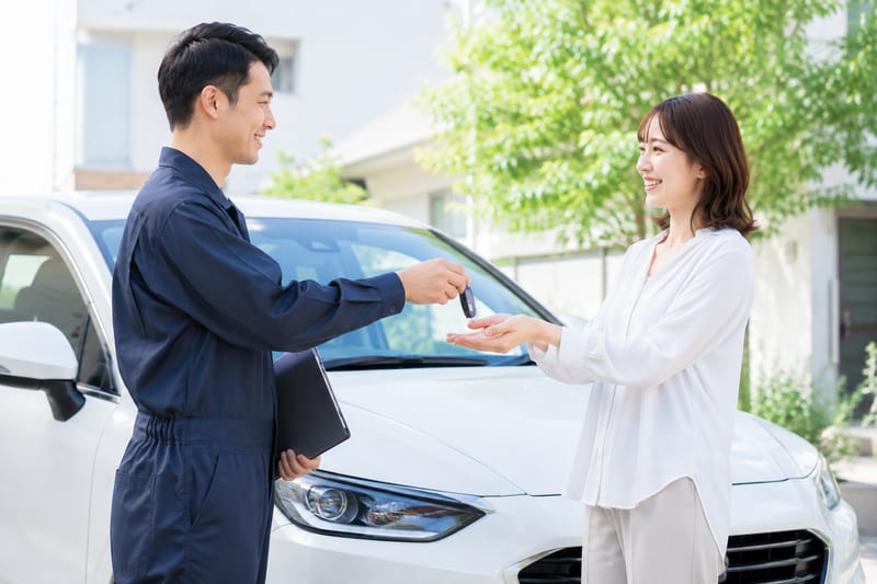 自宅の前で、買取店の担当者に愛車の鍵を手渡す女性
