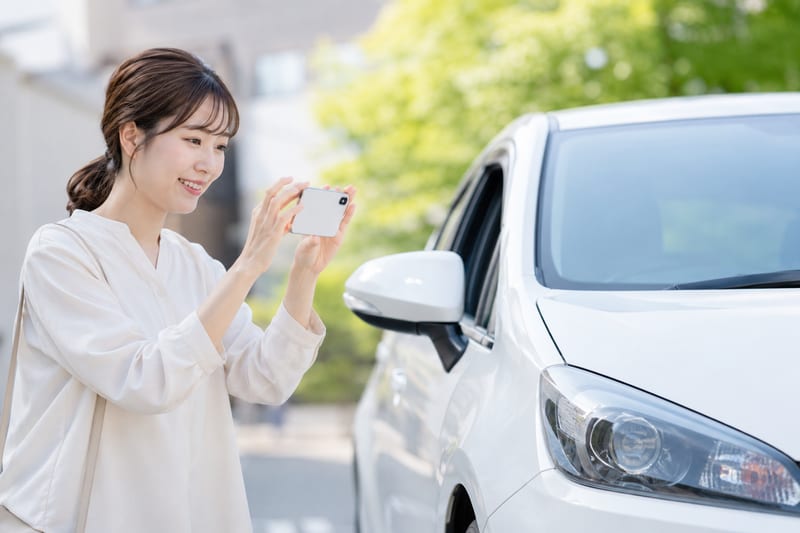 自宅の前でスマートフォンを構え、愛車の外観を撮影する女性